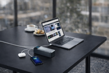 A close-up of an Anker 737 (PowerCore 24K) charging a laptop and smartphone on a table at an airport lounge, showcasing its 140W fast charging and smart digital display. 💻📱