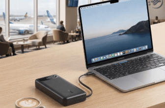 Black Anker A1383 87W power bank charging a silver MacBook on a wooden table in an airport lounge, sitting next to a cup of coffee.