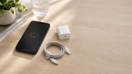 iphone not charging on a desk beside a USB-C charging cable and wall charger, screen showing a low battery